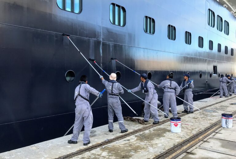 Coating crew painting a ship hull with roller poles