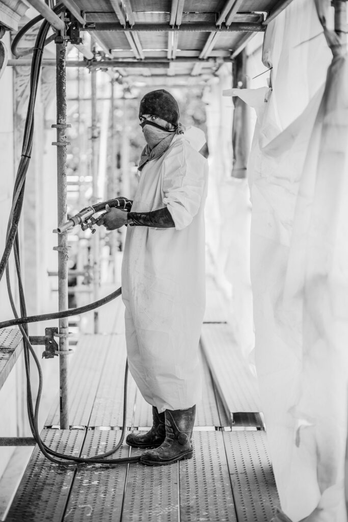 A worker in a protective suit spraying in a paint booth