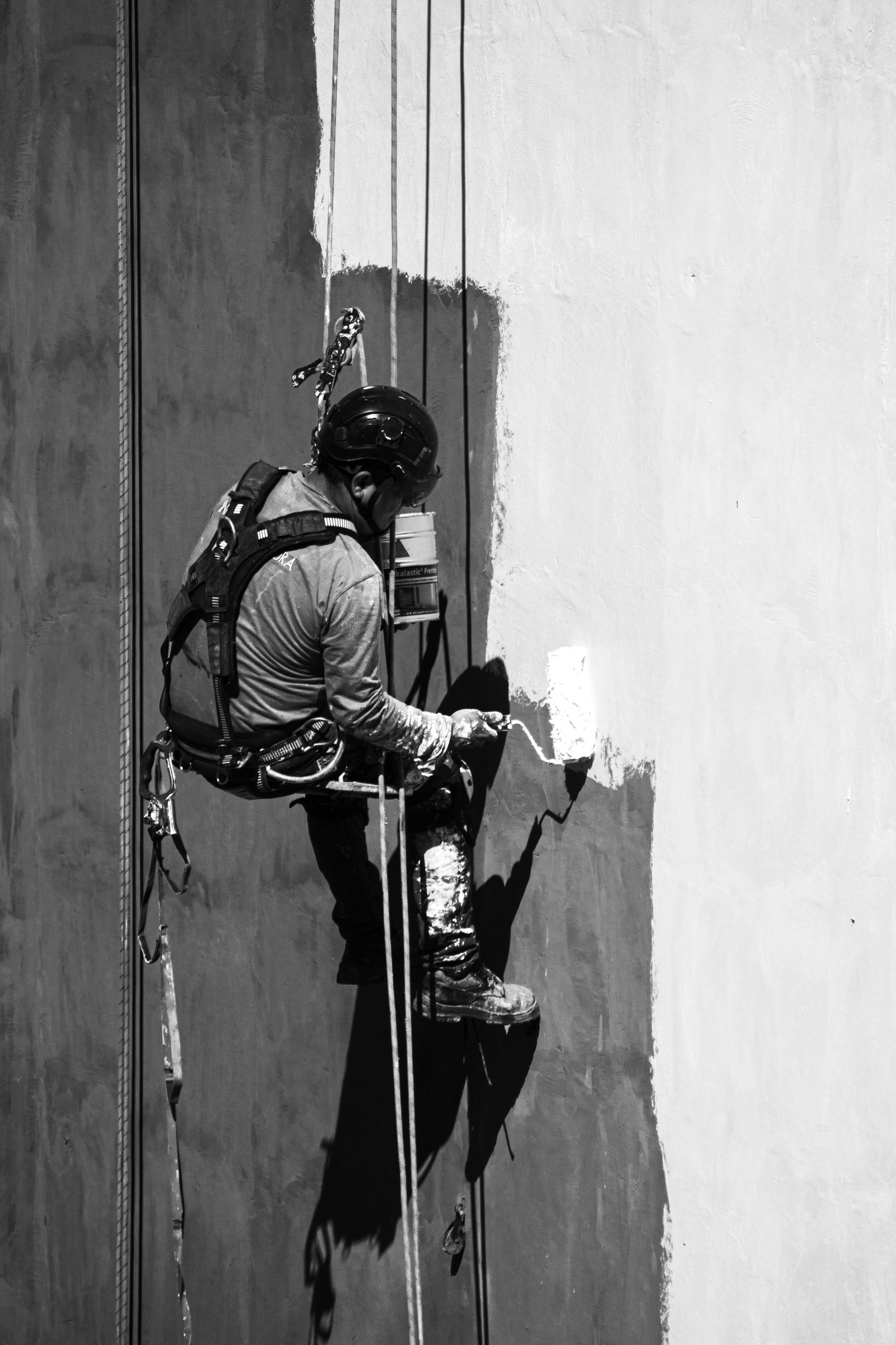 A rope access painter working a facade from ropes in harness and helmet