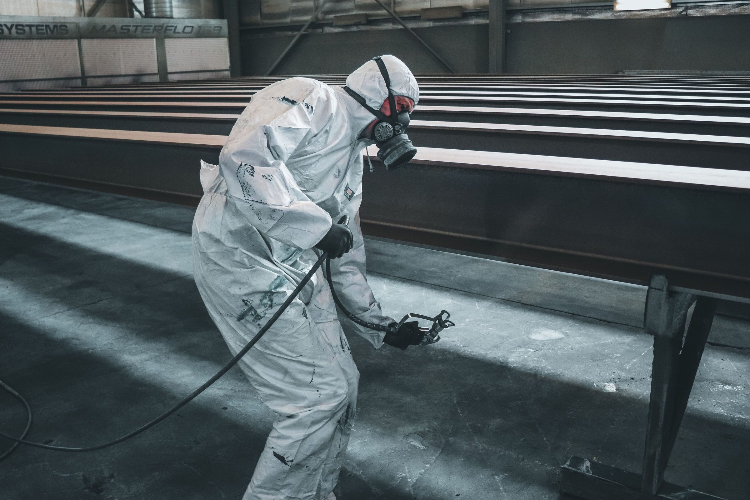 A sprayer in protective suit and respirator coating structural beams