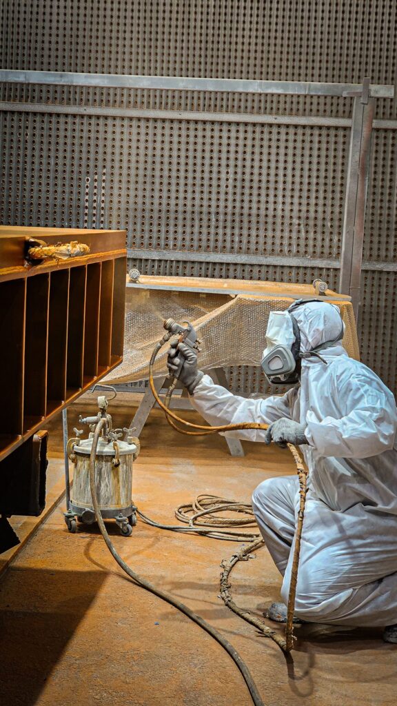 A sprayer in a full suit and respirator coating fabricated steelwork
