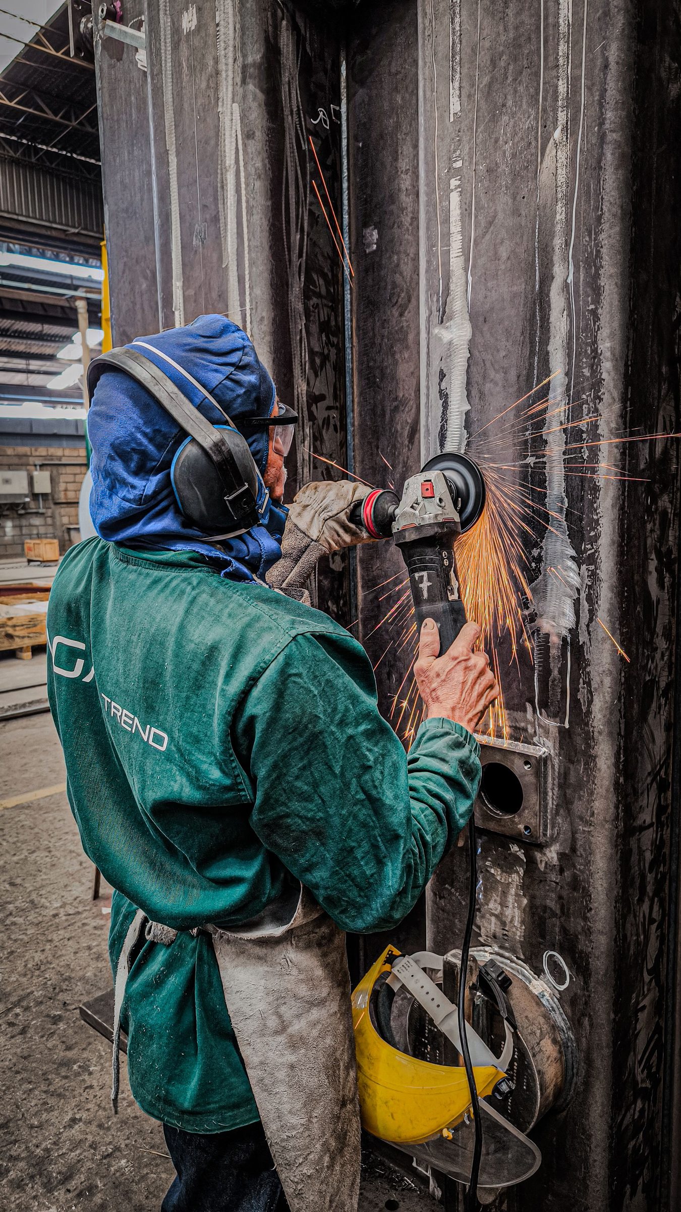 A worker in a respirator and ear defenders grinding a surface before coating